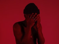 a man covering his face with his hands in front of a red background